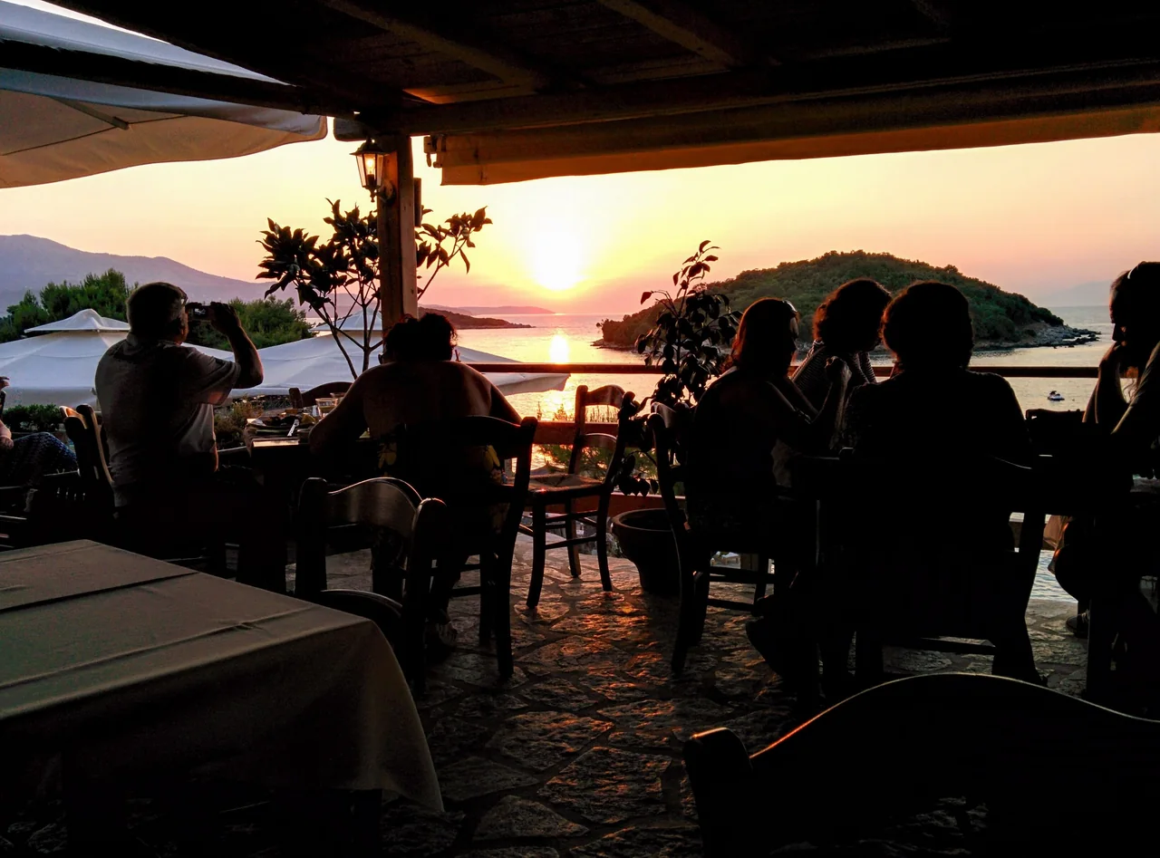 Gäste verbringen einen gemeinsamen Abend in einem Restaurant am Meer in Ksamil, während die Sonne über dem Wasser untergeht