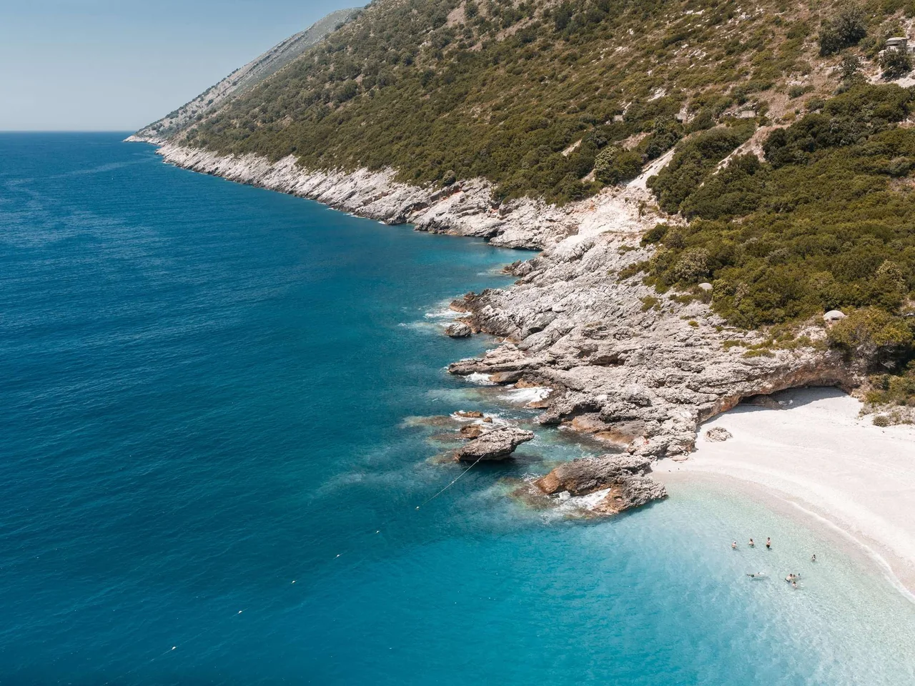 Türkisfarbenes Wasser des Ionischen Meeres an weißen Buchten und grünen Hügeln der Albanischen Riviera