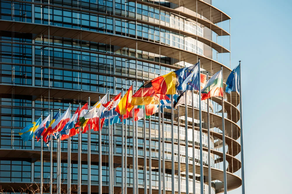 Europäische Flaggen vor einem modernen institutionellen Gebäude mit Glasfassade