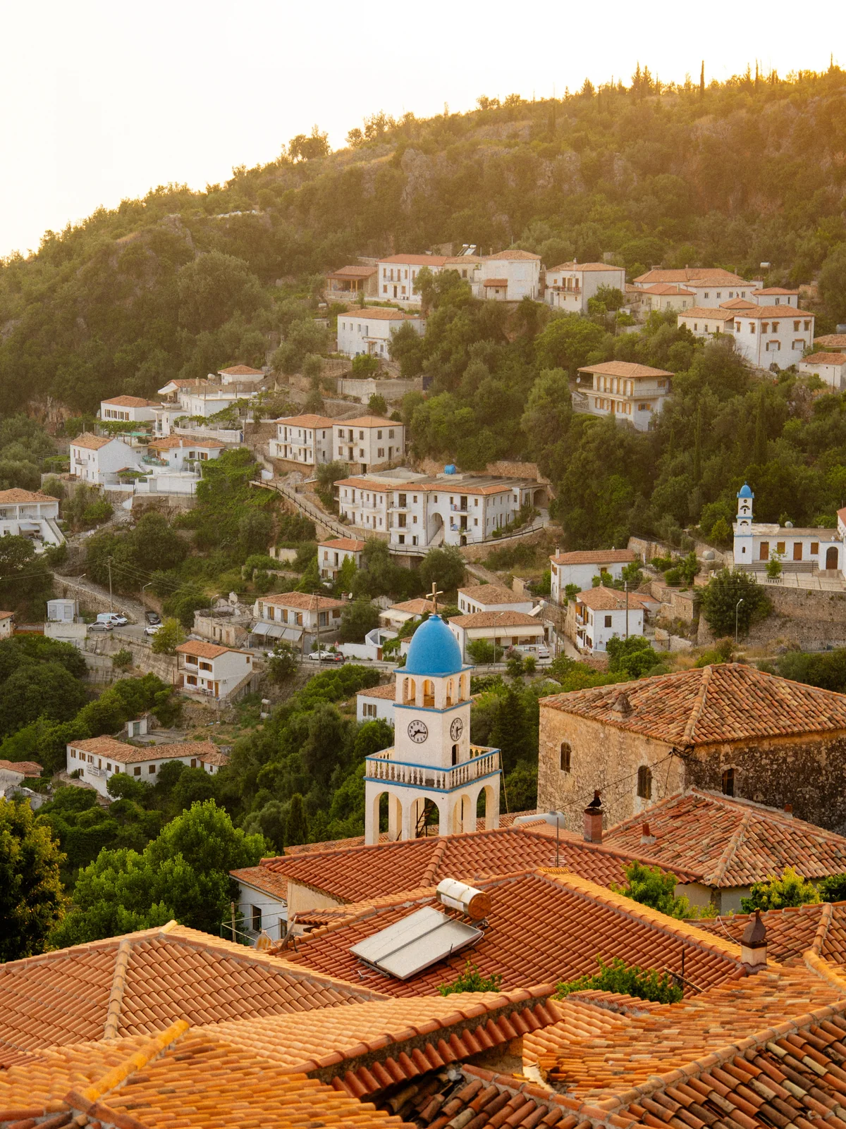 Mediterranes Bergdorf mit Terrakottadächern und blau bekuppelten Glockentürmen im goldenen Sonnenlicht
